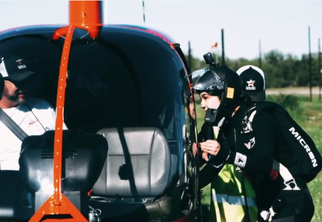 Person in helmet and gear talks to helicopter pilot through open door