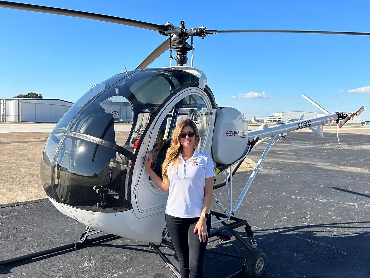 Person standing beside a parked helicopter on an airport tarmac under a clear blue sky.