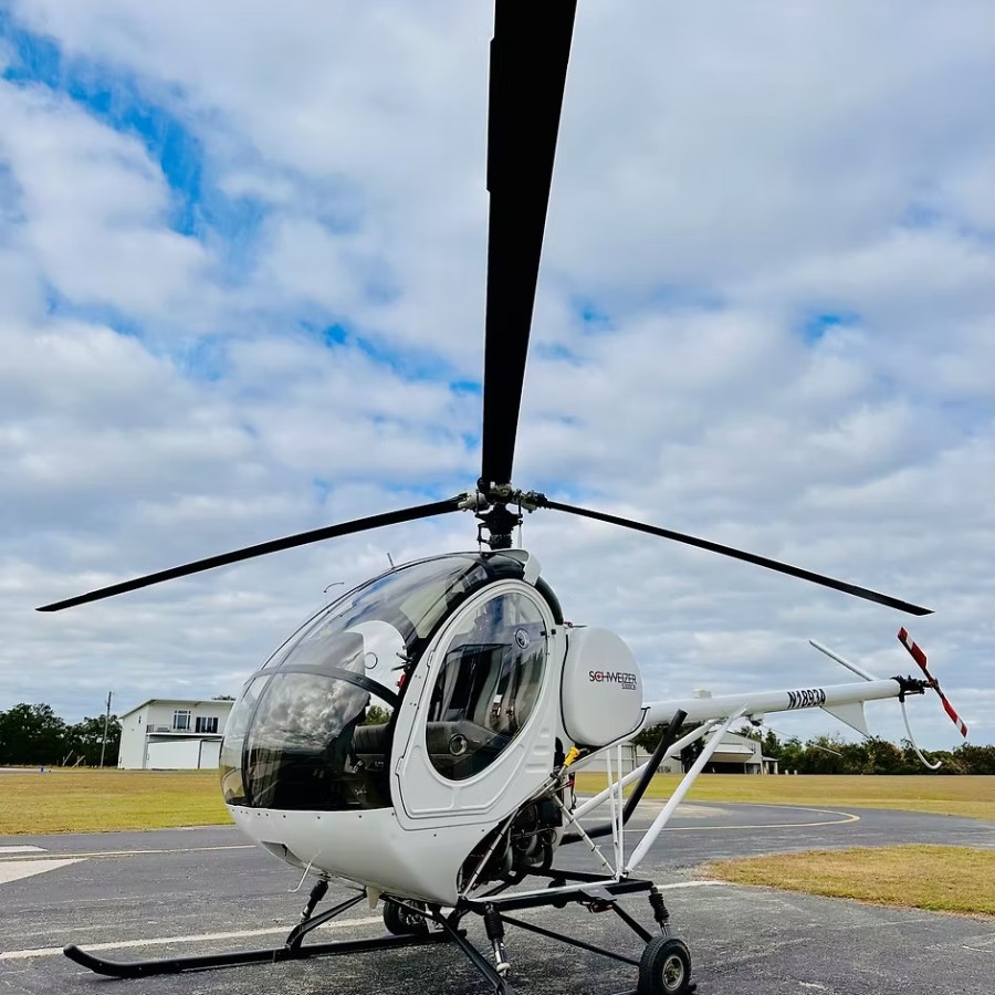 White helicopter parked on a tarmac under a cloudy sky.